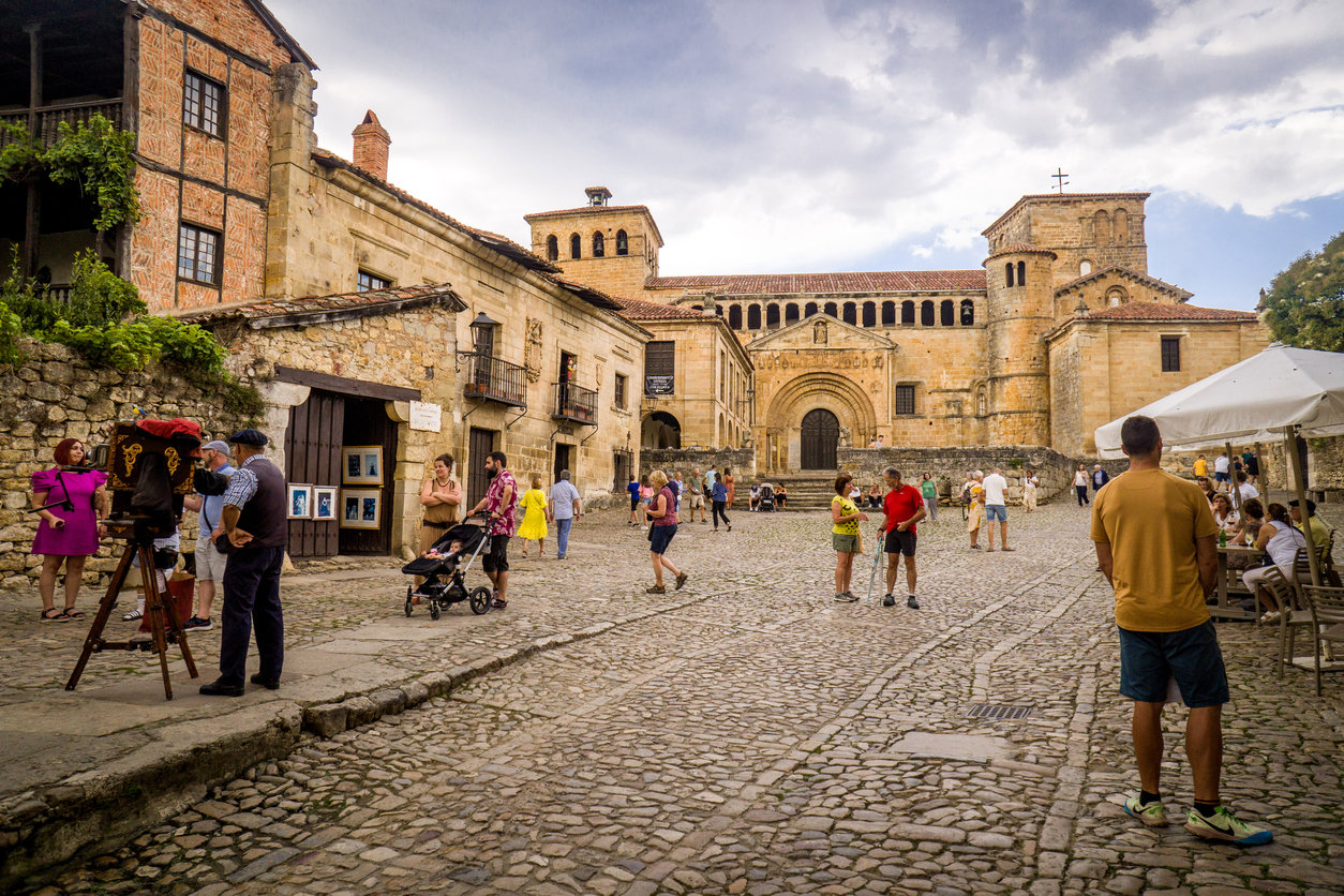 main square of the medieval town of santillana del mar with tourists walking by day and the collegiate church of santa juliana in the background